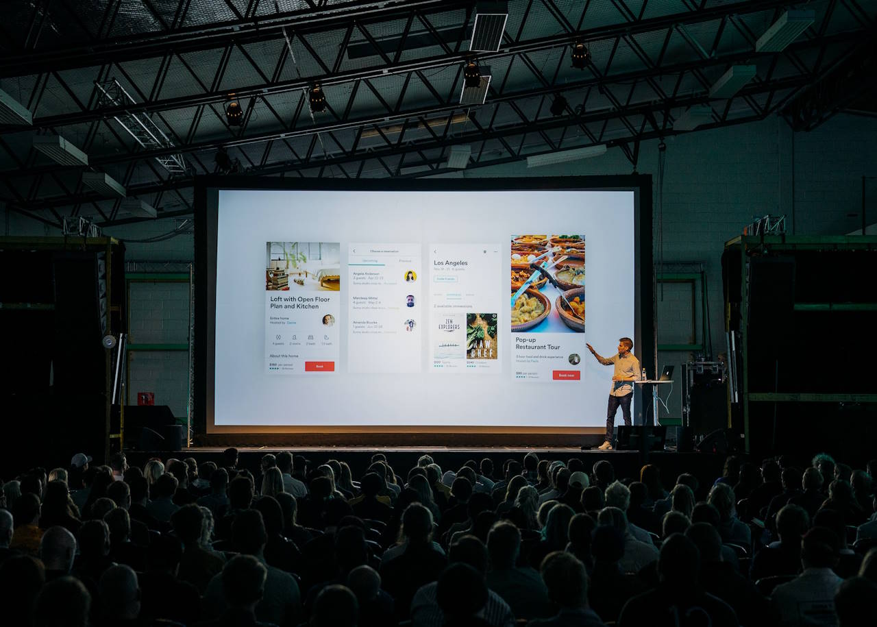 A man presenting at a conference, in a packed hall